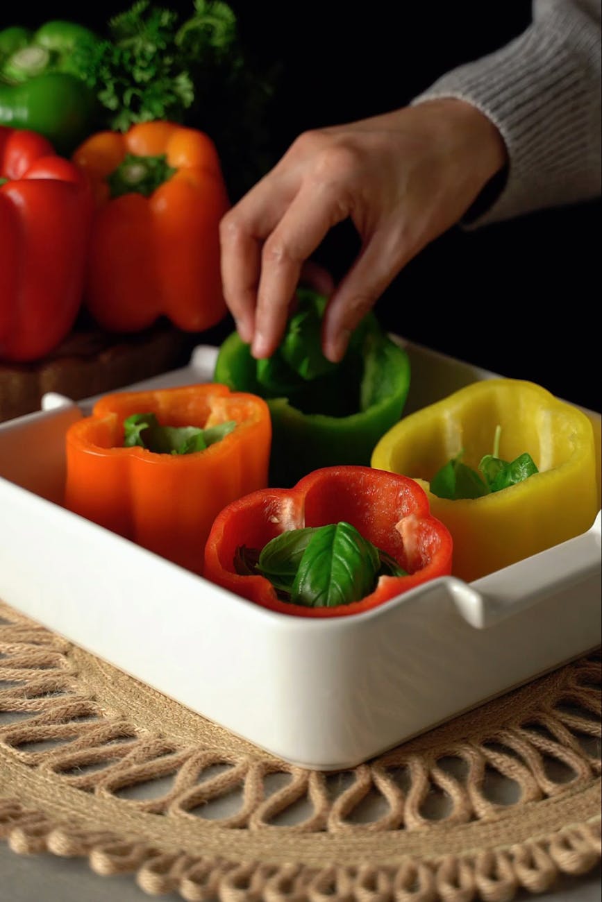 close up of a person putting basil leaves inside the peppers on a tray