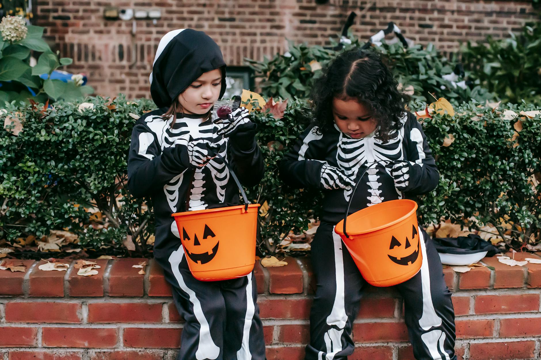 little multiracial girls in skeleton costumes sitting with candy bucket