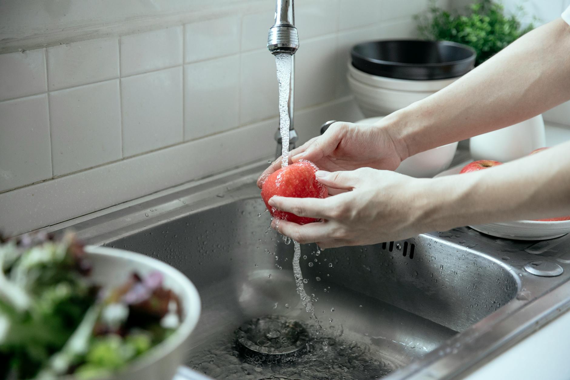 person washing a fruit from a faucet
